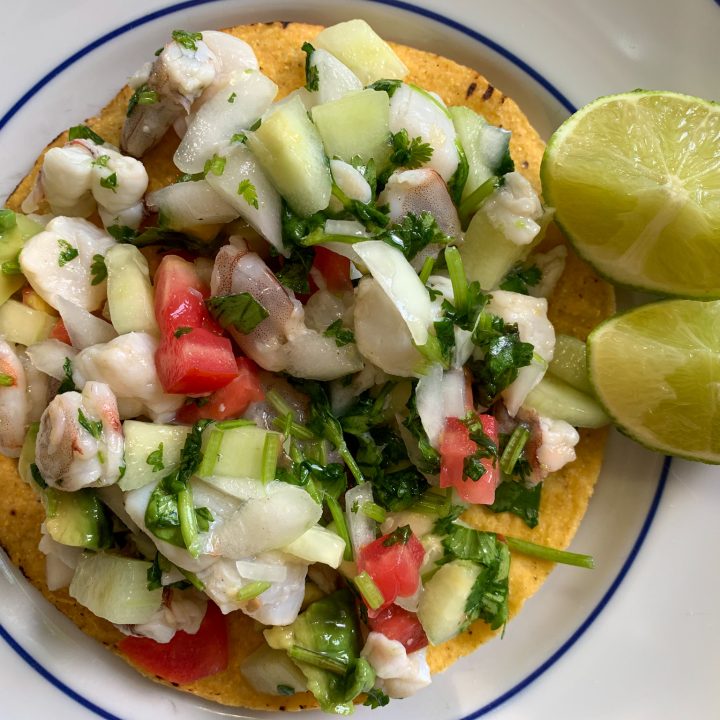 shrimp ceviche tostada on a plate with two sliced limes