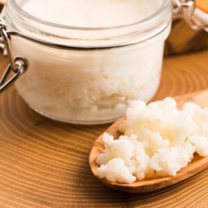 milk kefir grains in a glass jar and on a wooden spoon