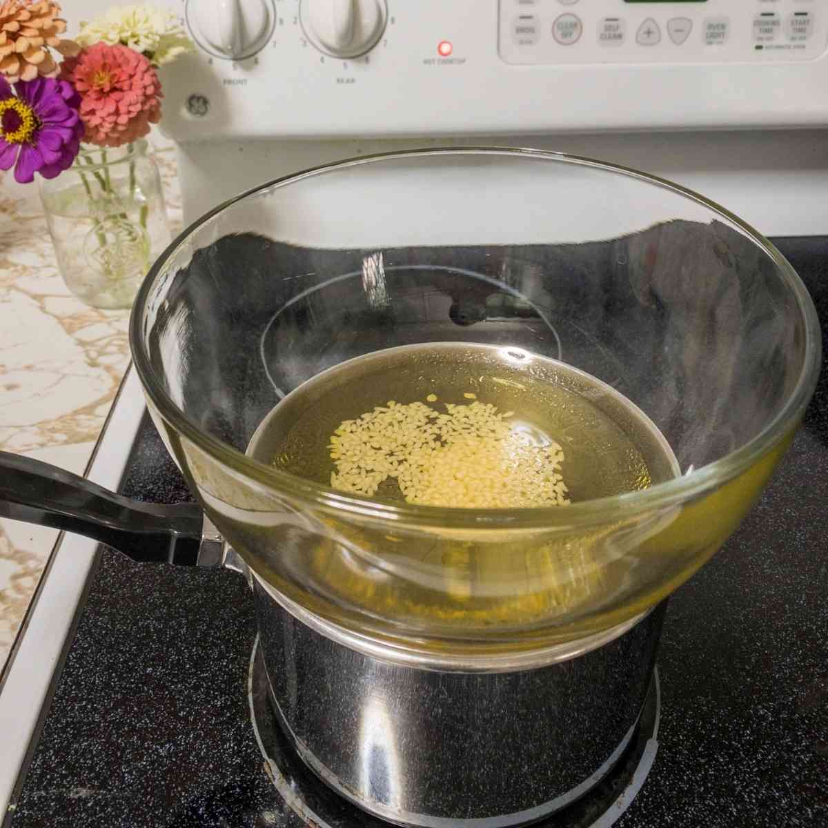 melting beeswax with avocado oil in a makeshift double boiler on the stove top to make breast milk lotion.