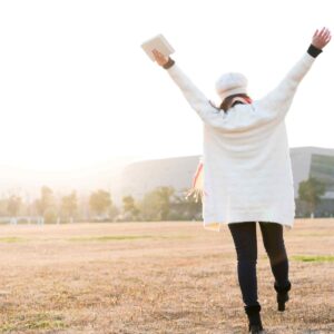 woman walking through a field worshipping God with arms extended to the heavens