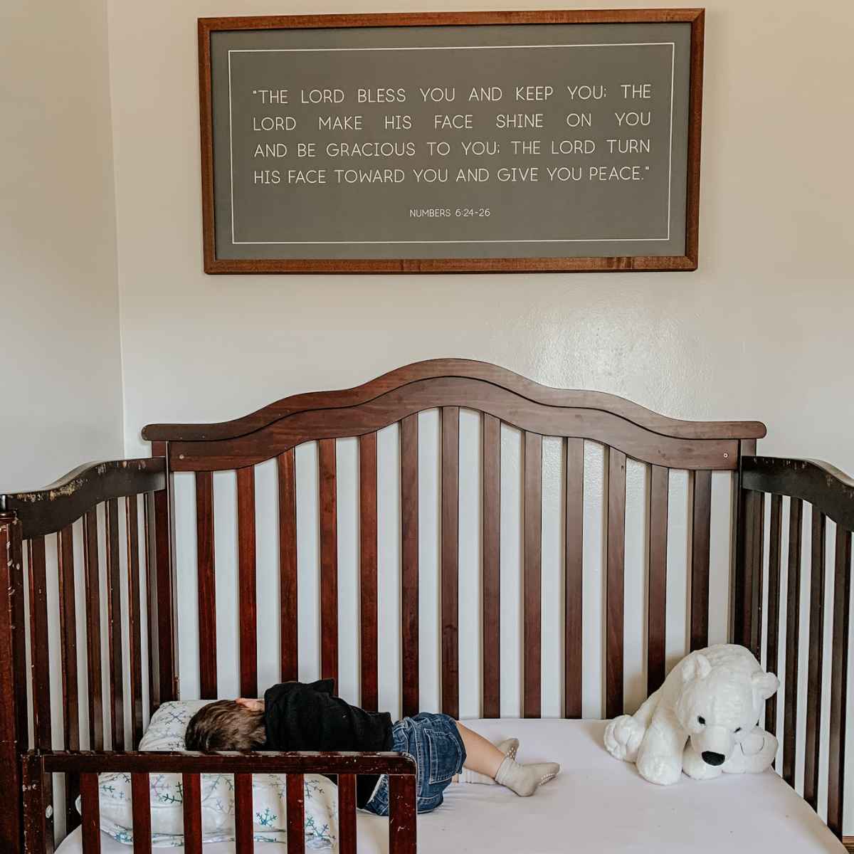 baby boy sleeping in his crib with the verses form numbers 6:24-26 framed above his crib.