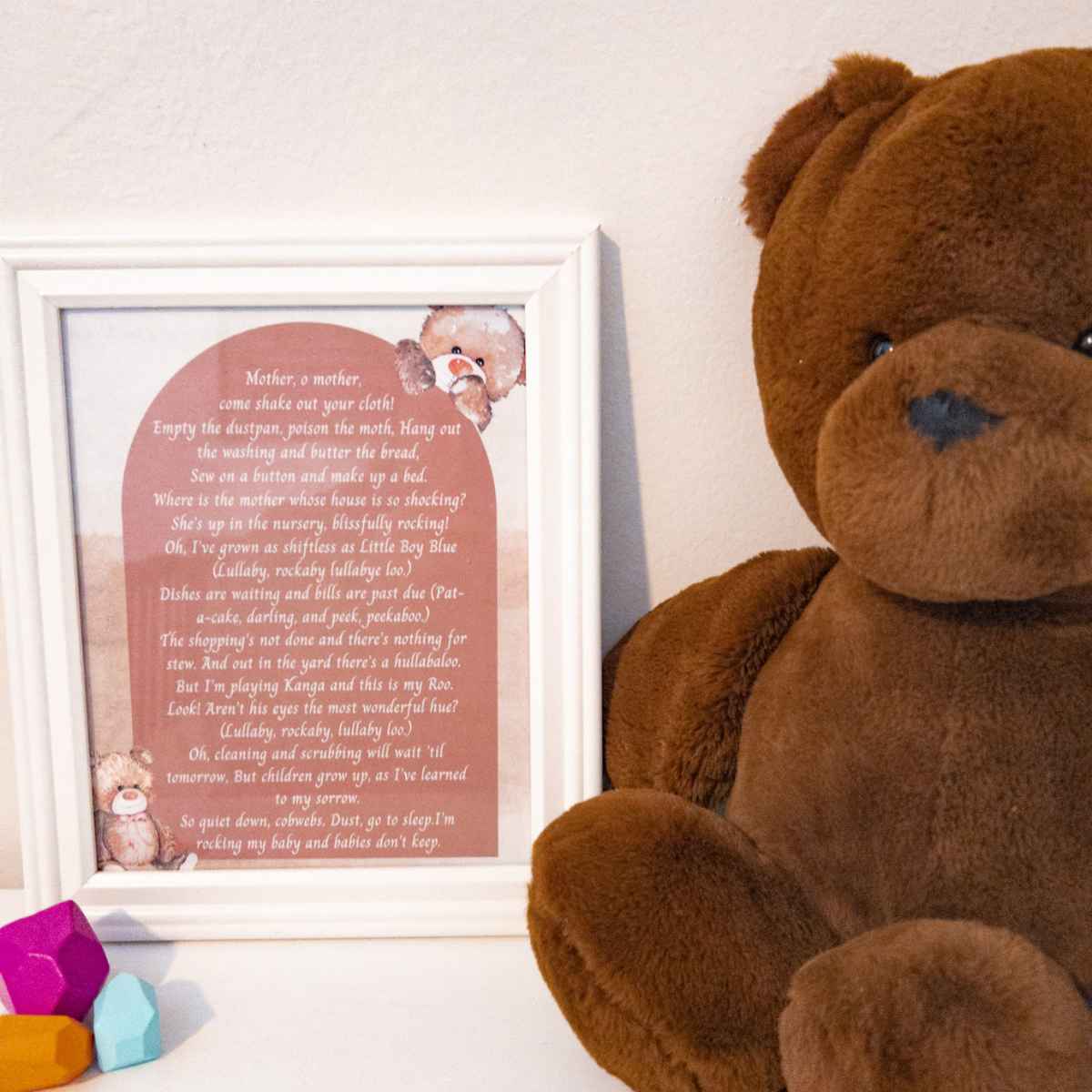 framed copy of the babies don't keep poem next to a teddy bear and wooden rocks