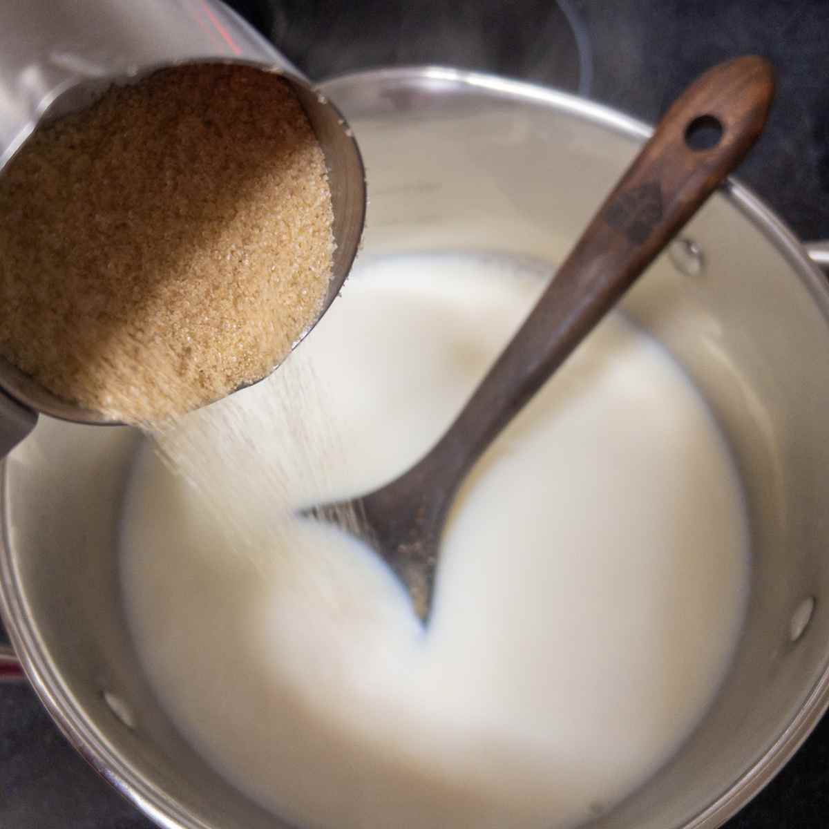 adding brown sugar to the warm milk in a 3qt pot