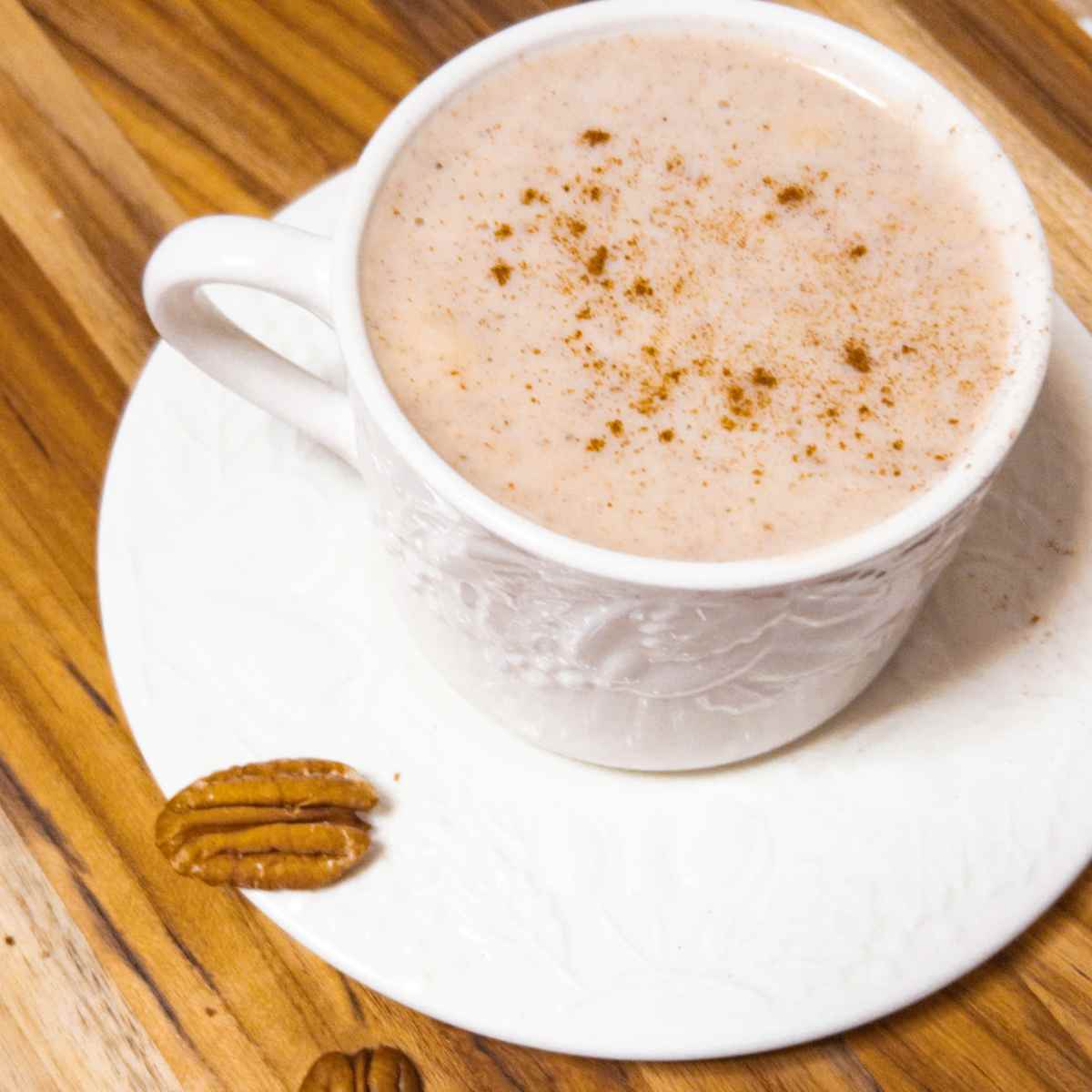 mug on a saucer with warm atole de nuez and a pecan on the side